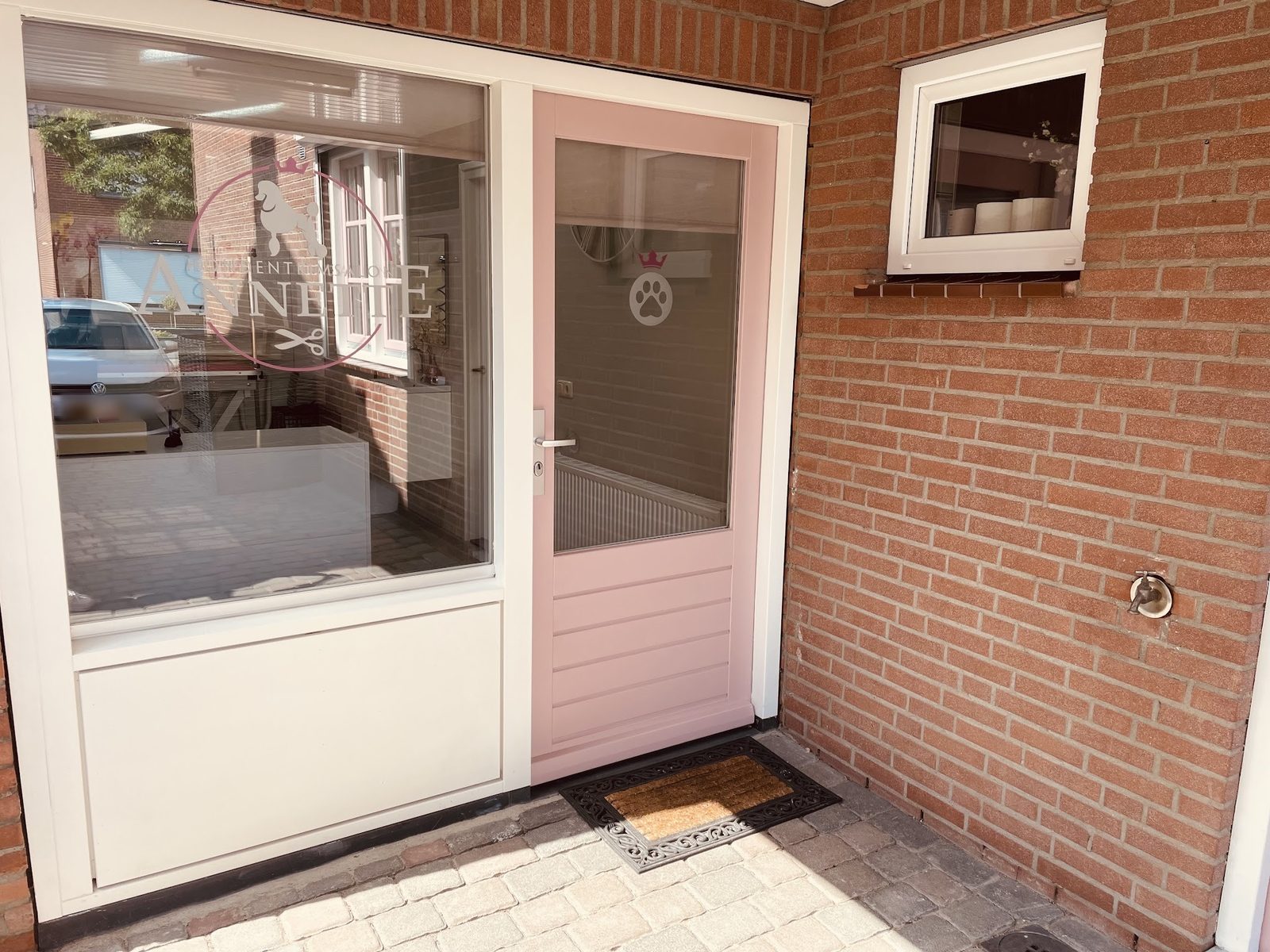 De roze deur van de salon met het logo van Hondentrimsalon Annette op het raam